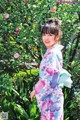 A woman in a kimono standing in front of a bush.