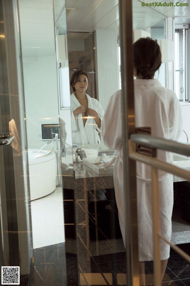 A woman in a white robe standing in front of a mirror.